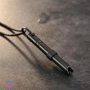 May include: A black pendant necklace featuring a cylindrical pendant with a curved end. The pendant is attached to a black chain. The necklace is made of metal and has a sleek, modern design. The pendant has a textured band.
