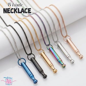 May include: A collection of whistle necklaces in various colors, including silver, black, gold, and iridescent. Each necklace features a small, cylindrical whistle pendant suspended from a matching chain. The text "Whistle Necklace" is displayed at the top.
