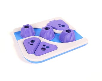 Op de afbeelding: Een blauw en wit puzzelspeeltje met verschillende paarse onderdelen. Het speelgoed bevat drie kleine, ronde, gegroefde stukjes en twee grotere, driehoekige stukjes, allemaal met kleine zeshoekige uitsparingen aan de bovenzijde.