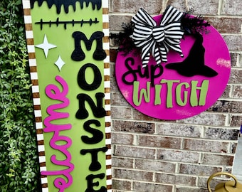 Puede incluir: Carteles de madera con temática de Halloween. Uno es un rectángulo verde largo con las palabras "Welcome Monsters" en negro y rosa. El otro es un círculo rosa con un sombrero de bruja y las palabras "Sup Witch" en verde.