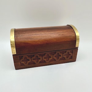 May include: A wooden box with a curved top and brass trim. The box is a rich brown color and features a carved floral design on the front. The box is closed and appears to be empty.