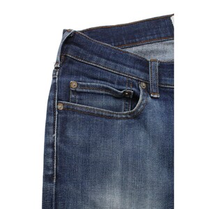 May include: Dark blue denim jeans featuring a classic five-pocket construction with a coin pocket, copper-toned metal rivets, and visible stitching along the seams. The fabric displays a subtle faded wash effect across the front panel.