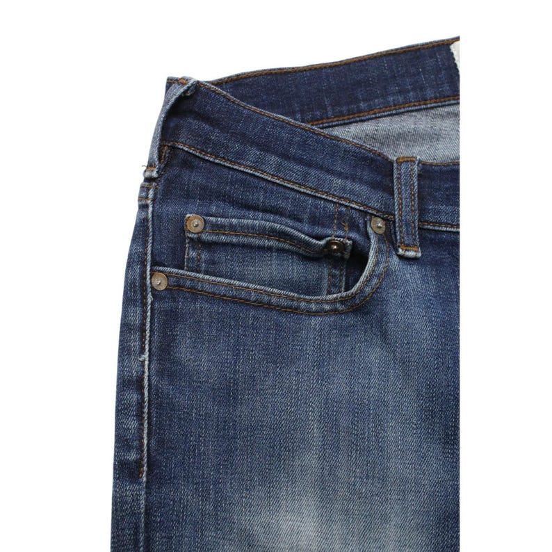 May include: Dark blue denim jeans featuring a classic five-pocket construction with a coin pocket, copper-toned metal rivets, and visible stitching along the seams. The fabric displays a subtle faded wash effect across the front panel.
