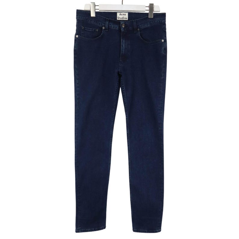 Pu&ograve; includere: Un paio di jeans in denim blu scuro caratterizzati da un classico design a cinque tasche, chiusura con bottoni e un'etichetta bianca del marchio sulla cintura interna con la scritta Acne Studios. I jeans hanno un taglio dritto e rivetti in metallo argentato.
