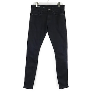 Könnte beinhalten: Eine dunkel anthrazitfarbene Jeans aus Denim mit klassischem Fünf-Taschen-Design, Knopf- und Reißverschluss sowie einer schmalen Passform. Die Jeans hängt an einem weißen Kleiderbügel und zeigt eine saubere, einfarbige Stoffoberfläche.