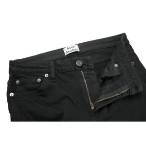 May include: Black denim jeans featuring a metal button fly closure, silver-toned rivets, and a white interior waistband label with the text Acne Studios. The garment includes a standard five-pocket design with visible stitching along the seams.