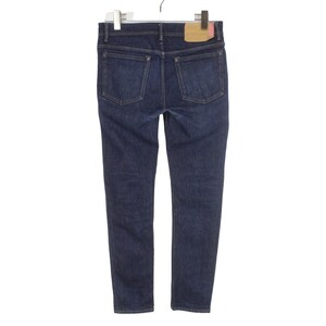 May include: Dark blue denim jeans featuring a classic five-pocket design with metal rivets at the corners of the back pockets. A rectangular tan leather-like patch is stitched onto the back waistband, and the garment is suspended from a hanger.