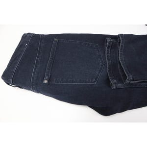 Pode incluir: Um par de cal&ccedil;as de ganga em cinzento carv&atilde;o escuro com um design cl&aacute;ssico de cinco bolsos, costuras vis&iacute;veis ao longo das bordas, um c&oacute;s estruturado com presilhas e rebites met&aacute;licos que refor&ccedil;am os cantos dos bolsos traseiros.