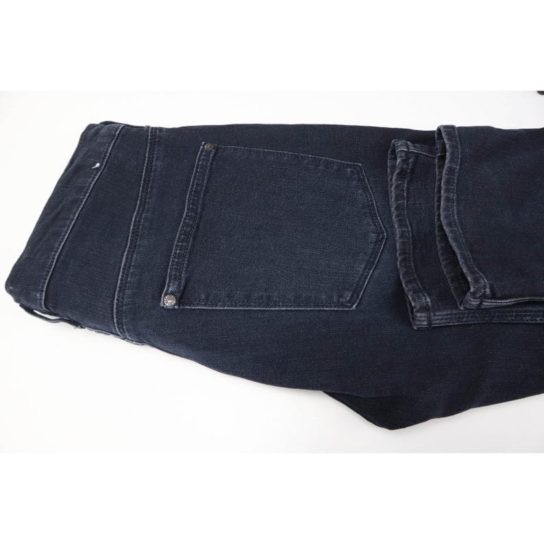 Pode incluir: Um par de cal&ccedil;as de ganga em cinzento carv&atilde;o escuro com um design cl&aacute;ssico de cinco bolsos, costuras vis&iacute;veis ao longo das bordas, um c&oacute;s estruturado com presilhas e rebites met&aacute;licos que refor&ccedil;am os cantos dos bolsos traseiros.