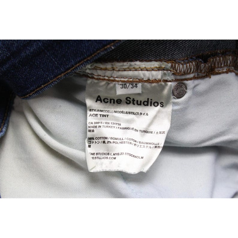 May include: A pair of dark blue denim jeans featuring an interior white fabric care label. The label displays the text Acne Studios, Ace Tint, 30/34, Made in Turkey, and indicates a composition of 98 percent cotton and 2 percent polyester.
