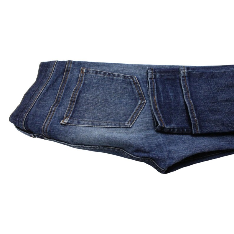 May include: A pair of folded blue denim jeans featuring a classic five-pocket design with a medium wash, visible stitching along the seams, a structured waistband, and a rectangular back pocket with reinforced edges and a faded texture.