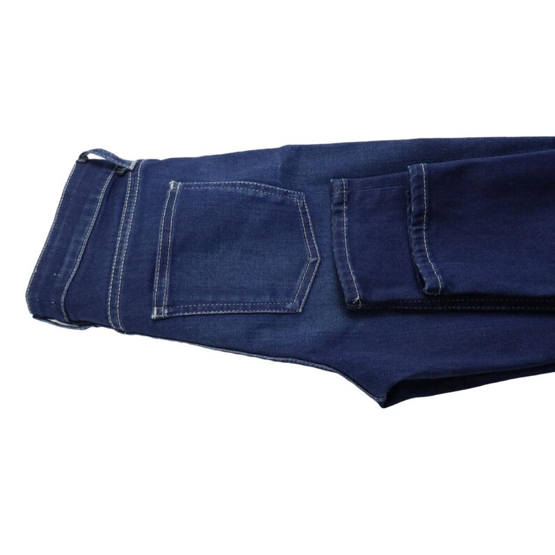 Puede incluir: Unos vaqueros de mezclilla azul oscuro con dise&ntilde;o de cintura alta, trabillas para cintur&oacute;n y un bolsillo trasero. La prenda est&aacute; confeccionada con costuras blancas en contraste a lo largo de los bordes de las costuras y bolsillos.