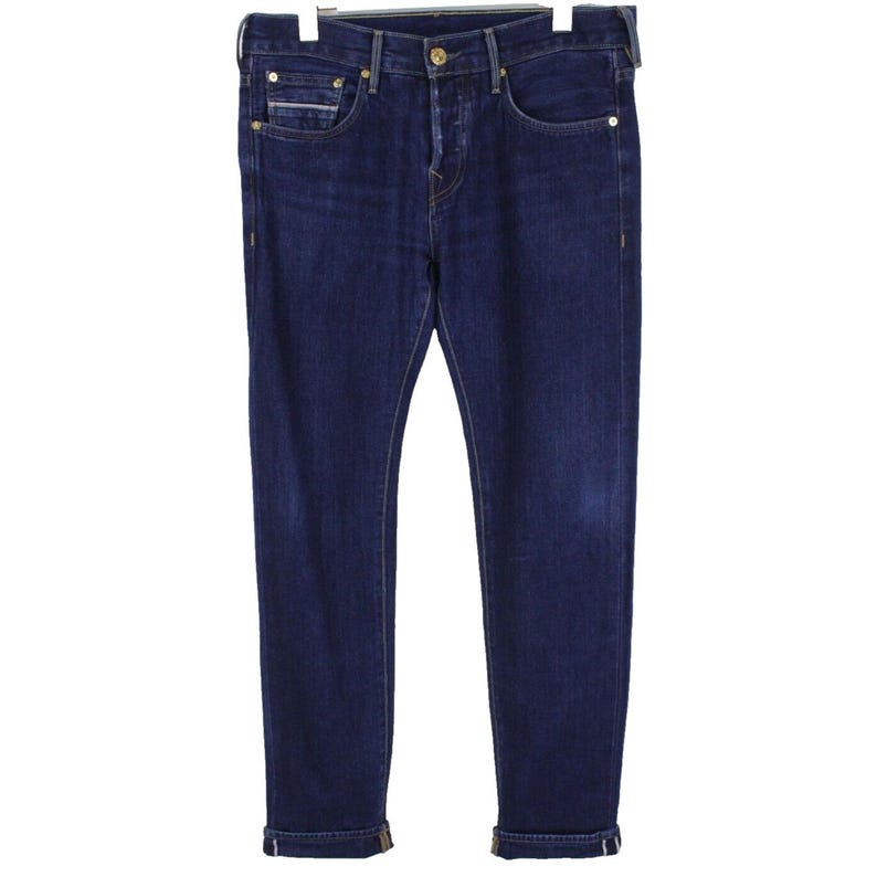 May include: Dark blue denim jeans featuring a classic five-pocket design, a button fly closure, and metallic rivets. The legs are tapered with rolled cuffs at the bottom, showcasing a lighter interior fabric edge along the hemline.
