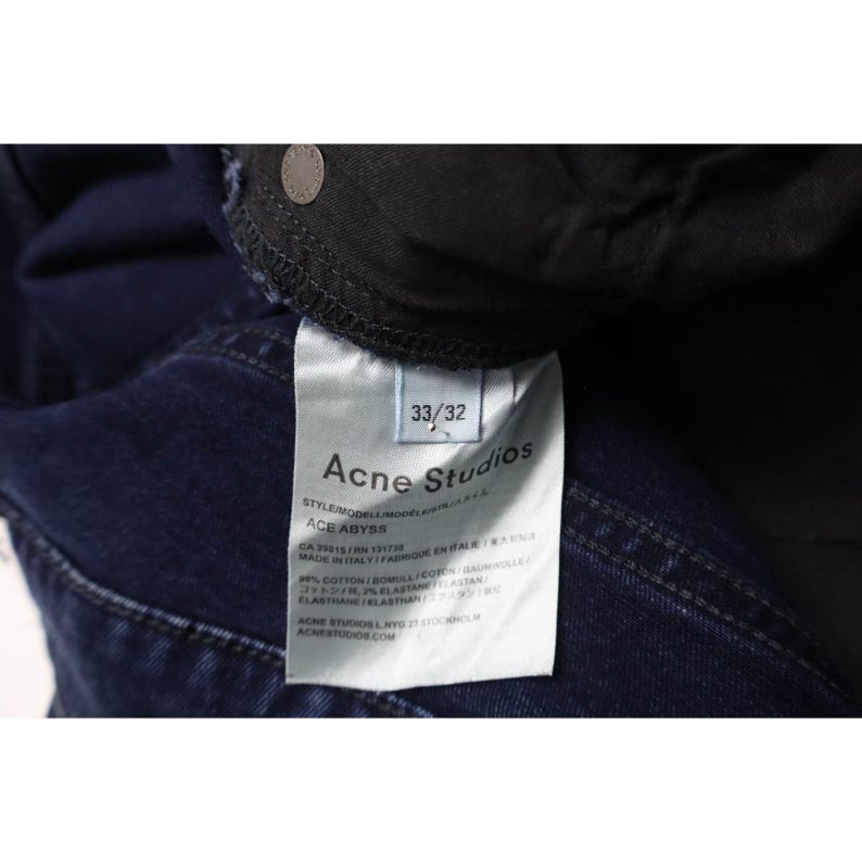 Pu&ograve; includere: Jeans in denim blu scuro con un'etichetta interna riportante il testo Acne Studios, Ace Abyss e la taglia 33/32. L'etichetta indica una composizione di 98% cotone e 2% elastan, con dettagli di produzione che indicano Made in Italy.