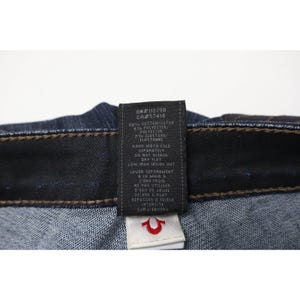 Peut inclure: Jean en denim bleu fonc&eacute; avec une &eacute;tiquette d'entretien noire &agrave; l'int&eacute;rieur portant du texte blanc indiquant une composition de 92% coton, 6% polyester et 2% &eacute;lasthanne, ainsi que des instructions de lavage. Une petite &eacute;tiquette blanche est fix&eacute;e.