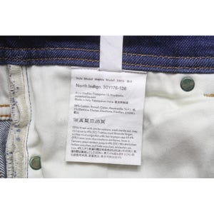 May include: A pair of dark blue denim jeans featuring a white interior care label. The label displays the text North Indigo, 30Y176-138, Acne Studios, and material composition of 98% cotton and 2% elastane, along with various laundry care symbols.