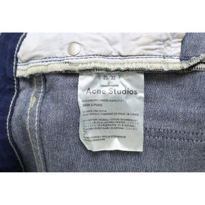 Puede incluir: Unos vaqueros de mezclilla azul con una etiqueta de cuidado blanca en el interior que muestra el texto Acne Studios, Skin 5 Pure, 25/32, y detalles de composici&oacute;n de 92% algod&oacute;n, 6% elastomultiester y 2% elastano, con un remache de metal plateado.