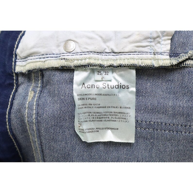 Puede incluir: Unos vaqueros de mezclilla azul con una etiqueta de cuidado blanca en el interior que muestra el texto Acne Studios, Skin 5 Pure, 25/32, y detalles de composici&oacute;n de 92% algod&oacute;n, 6% elastomultiester y 2% elastano, con un remache de metal plateado.