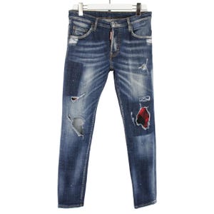 Może przedstawiać: Niebieskie dżinsy z denimu z przetarciami, w tym rozdarciami i łatami. Dżinsy mają klasyczny pięciokieszeniowy krój i wiszą na białym wieszaku. Łaty są w czerwono-czarną kratę.