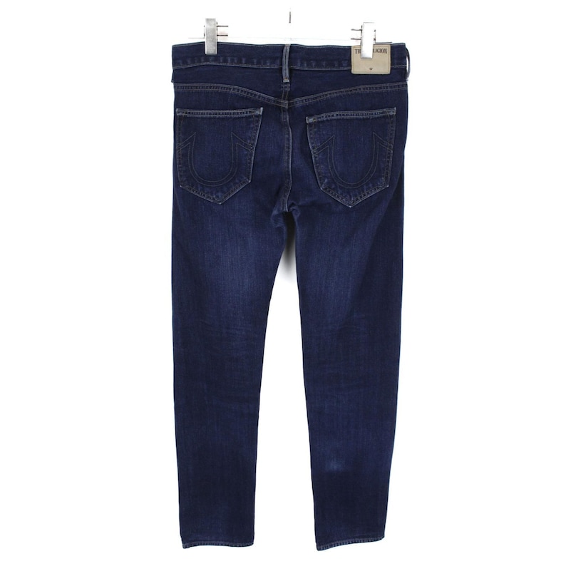 May include: Dark blue denim jeans featuring a classic five-pocket design with a button fly and belt loops. The back pockets display a signature horseshoe-shaped stitch pattern in a matching thread color. A light-colored leather brand patch is attached.