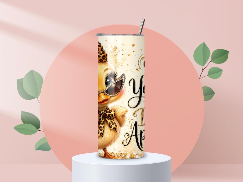 May include: A cylindrical stainless steel tumbler featuring a graphic of a yellow duckling wearing leopard print accessories, including a hat, bow, and sunglasses. The design includes gold glitter accents and black cursive text on a cream background.