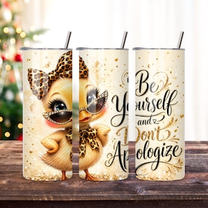 May include: A cylindrical stainless steel tumbler with a straw, featuring a cartoon duckling wearing a leopard print bow and sunglasses, surrounded by gold glitter accents and the black cursive text Be Yourself and Don't Apologize.