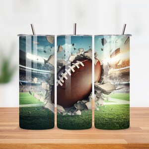 May include: Three stainless steel tumblers with lids and straws. Each tumbler features a different image of a football breaking through a wall of concrete. The football is brown and white.