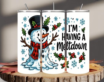 May include: A white tumbler featuring a cartoon snowman wearing a black top hat, red and black scarf, and a carrot nose. The tumbler has the text "I'M HAVING A Meltdown" with snowflakes and holly berry accents. A silver straw is visible.