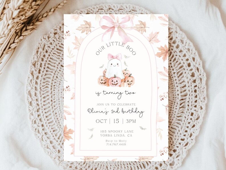 Op de afbeelding: Een uitnodigingskaart met Halloween-thema met een illustratie van een spook en pompoenen. De tekst luidt "Our Little Boo is turning two" met evenementdetails. Het ontwerp heeft een roze strik en herfstbladeren.