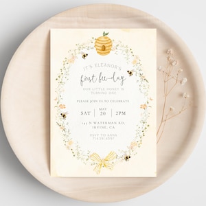 Peut inclure: Une invitation de fête de premier anniversaire sur le thème des abeilles jaunes et blanches avec une couronne de fleurs, un nid d'abeilles et des abeilles. Le texte indique "C'est le premier jour d'abeille d'Eleanor. Notre petit miel a un an. Veuillez vous joindre à nous pour célébrer. Sam 20 mai 14h. 145 N Waterman Rd. Irvine, CA. RSVP à Anna 714.391.4597"