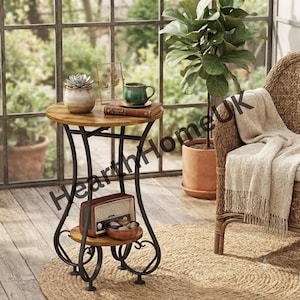 May include: A round side table with a wood-grain top and lower shelf, supported by black metal legs with scrollwork details. The table holds a small potted succulent, a green mug, a book, a vintage-style radio, and a bowl of stones.