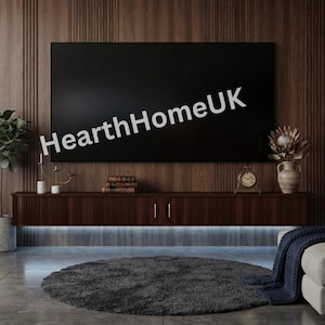 May include: A dark wood floating media console with vertical slats and gold handles mounted on a wood paneled wall beneath a large television screen displaying the text HearthHomeUK. The console features under-cabinet LED lighting.