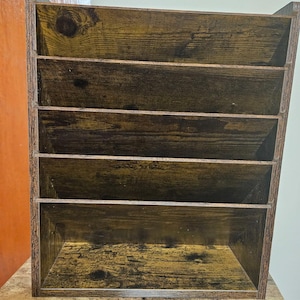 May include: A wooden desk organizer with five compartments. The organizer has a rustic, distressed finish with visible wood grain and knots. The color is a mix of brown and black.
