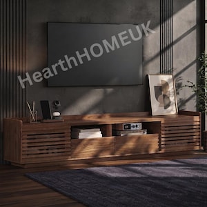 May include: A long, low-profile wooden media console featuring slatted cabinet doors on the ends and two central drawers. The unit has a rich brown wood grain finish and is positioned beneath a wall-mounted television with the text HearthHOMEUK.