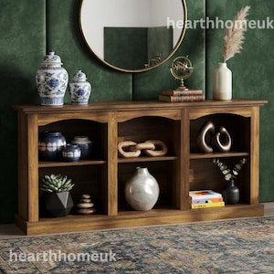 May include: A long wooden console table with three open shelving sections, featuring blue and white ceramic jars, a metallic armillary sphere, a large white vase, stacked books, a succulent in a geometric pot, and decorative wooden chain links.