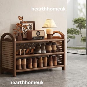 May include: A dark wood shoe rack with two shelves and woven cane side panels. The top shelf holds a brown radio, a framed picture, and a small lamp with a pleated shade. The shelves are filled with various pairs of shoes. Text reads hearthhomeuk.