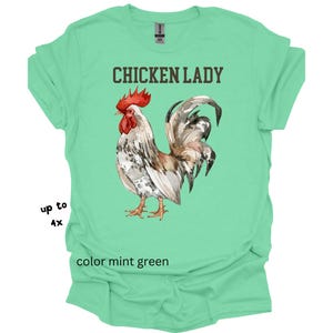 May include: Mint green t-shirt with the text "CHICKEN LADY" above a watercolor illustration of a rooster. The rooster has red, brown, white, and gray feathers. The shirt is available in sizes up to 4X.