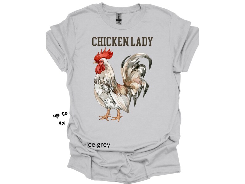 May include: Ice grey t-shirt featuring a watercolor illustration of a rooster with a red comb and wattle. The text "CHICKEN LADY" is printed above the rooster. The shirt is available in sizes up to 4X.