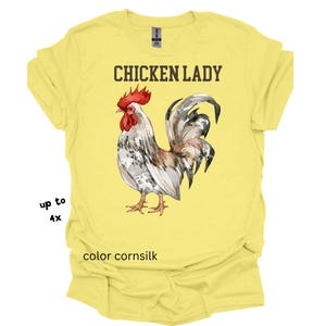 May include: A yellow t-shirt with the text "CHICKEN LADY" above a watercolor illustration of a rooster. The rooster has red, white, and gray feathers. The shirt is color cornsilk and available up to size 4X.