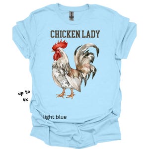 May include: Light blue t-shirt with the text "CHICKEN LADY" above a watercolor illustration of a rooster. The rooster has red, white, and brown feathers. The shirt is available in sizes up to 4X.