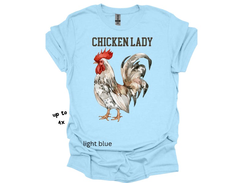 May include: Light blue t-shirt with the text "CHICKEN LADY" above a watercolor illustration of a rooster. The rooster has red, white, and brown feathers. The shirt is available in sizes up to 4X.