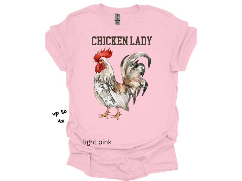 May include: Light pink t-shirt with the text "CHICKEN LADY" above a watercolor illustration of a rooster. The rooster has red, white, brown, and gray feathers. The shirt is available up to size 4X.