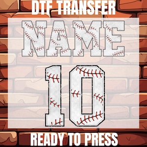 May include: White iron-on transfer with a baseball theme. The transfer features the word "NAME" and the number "10" with a baseball stitch design. The text "DTG TRANSFER" and "READY TO PRESS" are also included.
