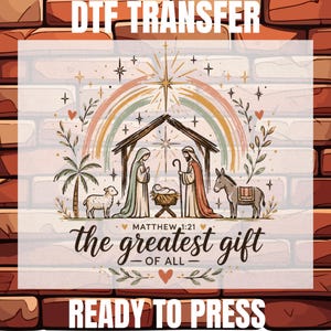May include: A DTF transfer featuring a nativity scene with a rainbow, a star, a palm tree, a sheep, and a donkey. The text reads DTF TRANSFER, MATTHEW 1:21, the greatest gift OF ALL, and READY TO PRESS. The design includes figures of Mary and Joseph.