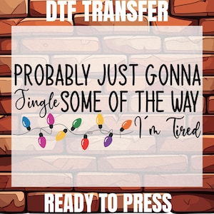 May include: A DTF transfer design with the text "PROBABLY JUST GONNA Jingle SOME OF THE WAY I'm Tired" in black script. A string of colorful Christmas lights is featured below the text. The words "DTF TRANSFER" and "READY TO PRESS" are also included.