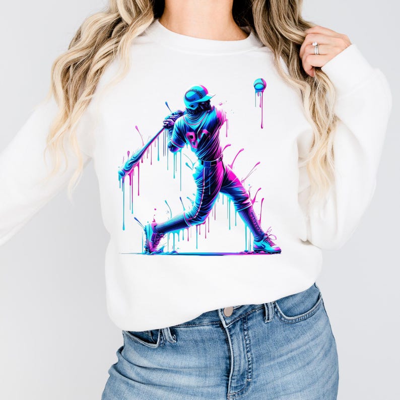 May include: White sweatshirt with a neon baseball player graphic. The design shows a batter mid-swing, with vibrant blue, pink, and purple dripping paint effects. The baseball and bat are also highlighted with neon colours.