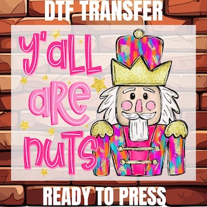 May include: A DTF transfer design featuring a colorful nutcracker with the text "y'all are nuts" in pink. The nutcracker wears a gold crown and a pink and teal jacket. The words "READY TO PRESS" are at the bottom.