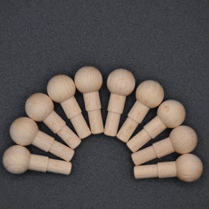 Może przedstawiać: Zestaw dziesięciu drewnianych kołków z zaokrąglonymi końcówkami. Kołki są ułożone w półkole na szarym tle.