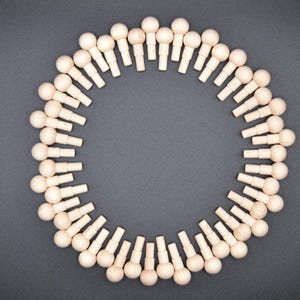 May include: A circular arrangement of small, light-colored wooden pegs with rounded tops, set against a dark gray background. The pegs are evenly spaced, forming a complete circle with an empty center. The pegs are likely for crafts.