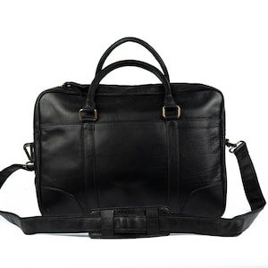 Peut inclure: Mallette en cuir noir avec poignées supérieures et bandoulière amovible. Le sac est doté d'une quincaillerie de couleur laiton et d'une forme rectangulaire. La mallette a une poche avant et une poche arrière.